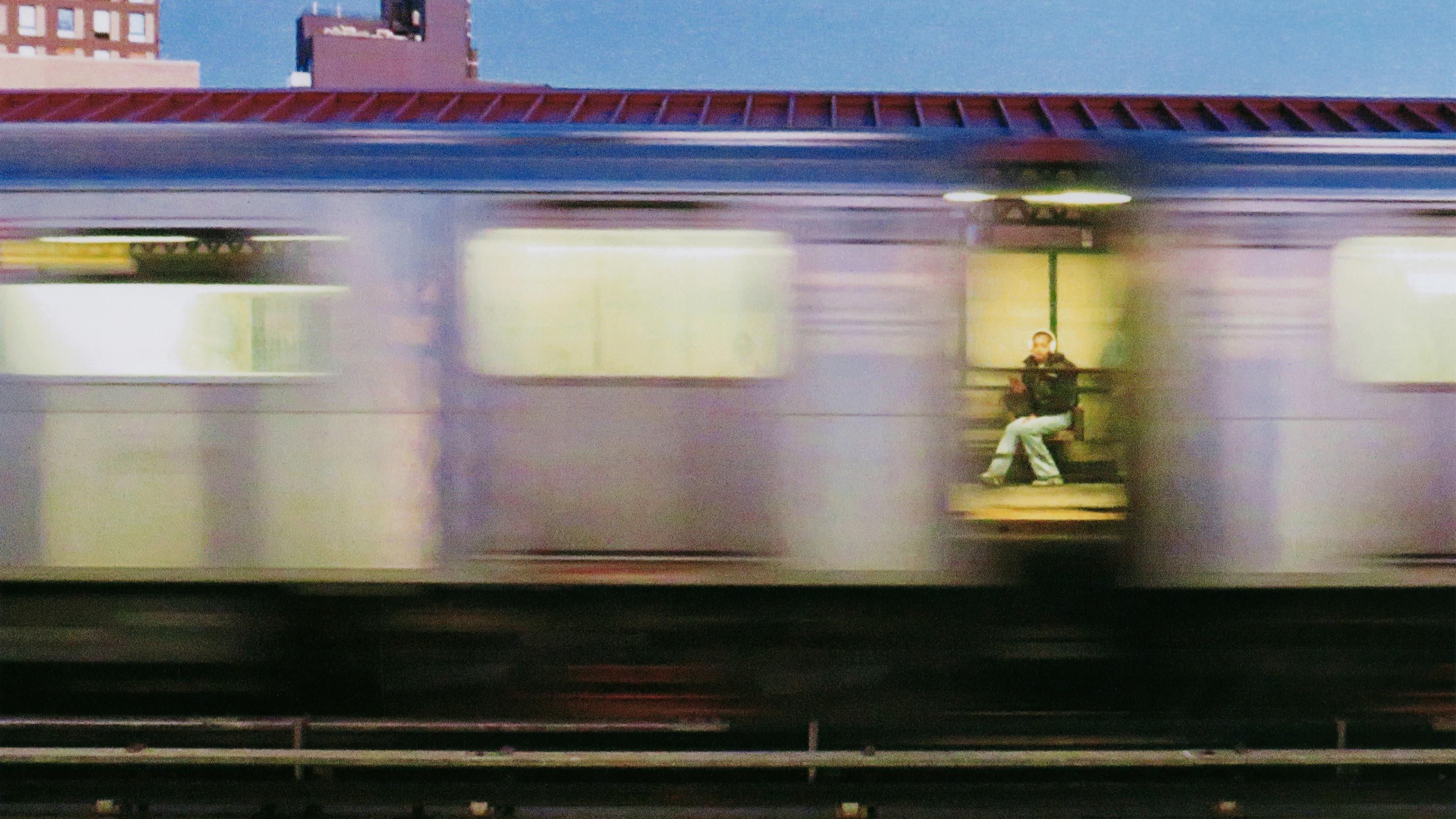 Moving photo image of a train, and in the between carts sits a woman.