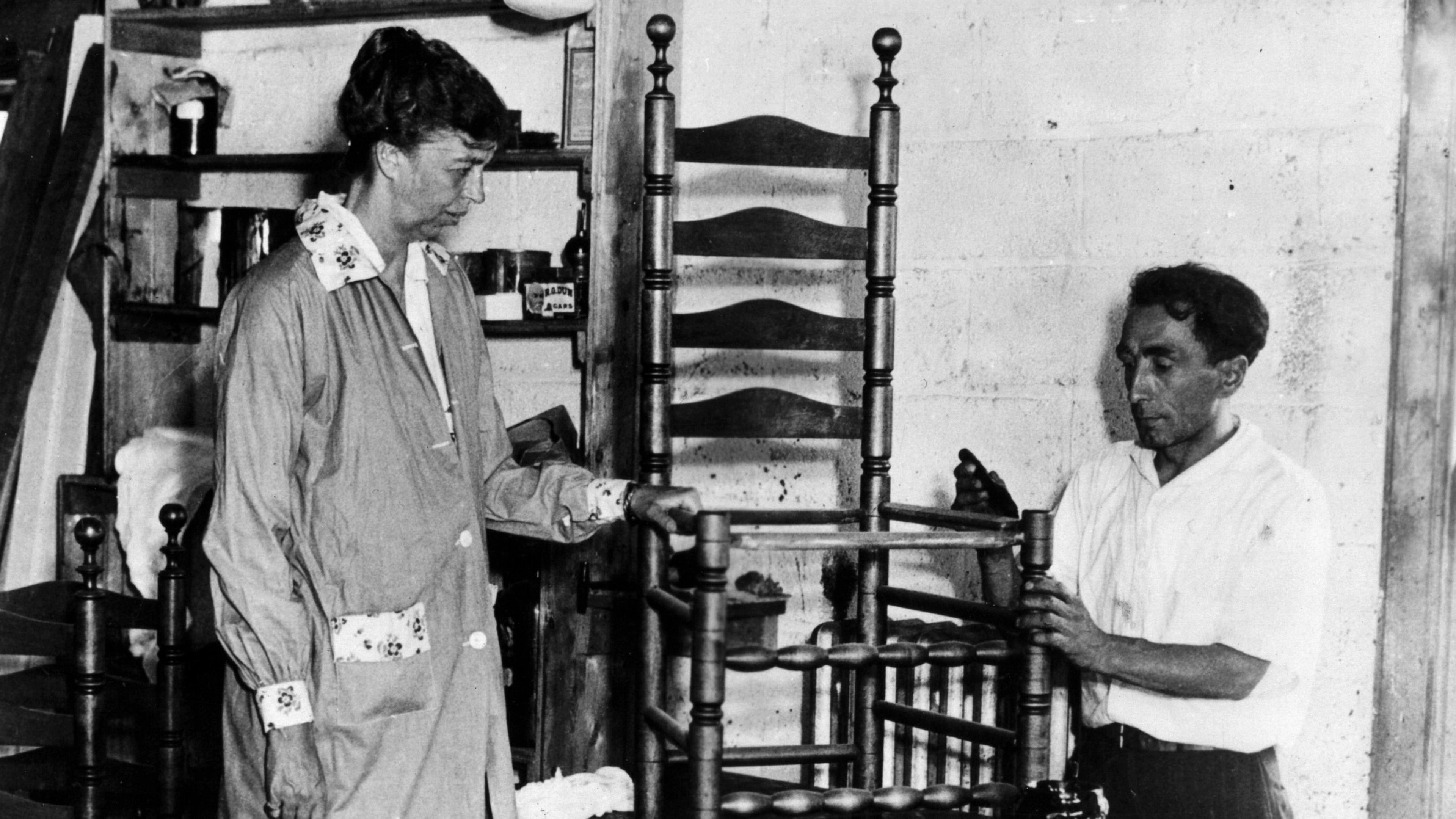 Black and white photo of a man and woman fixing a wooden chair
